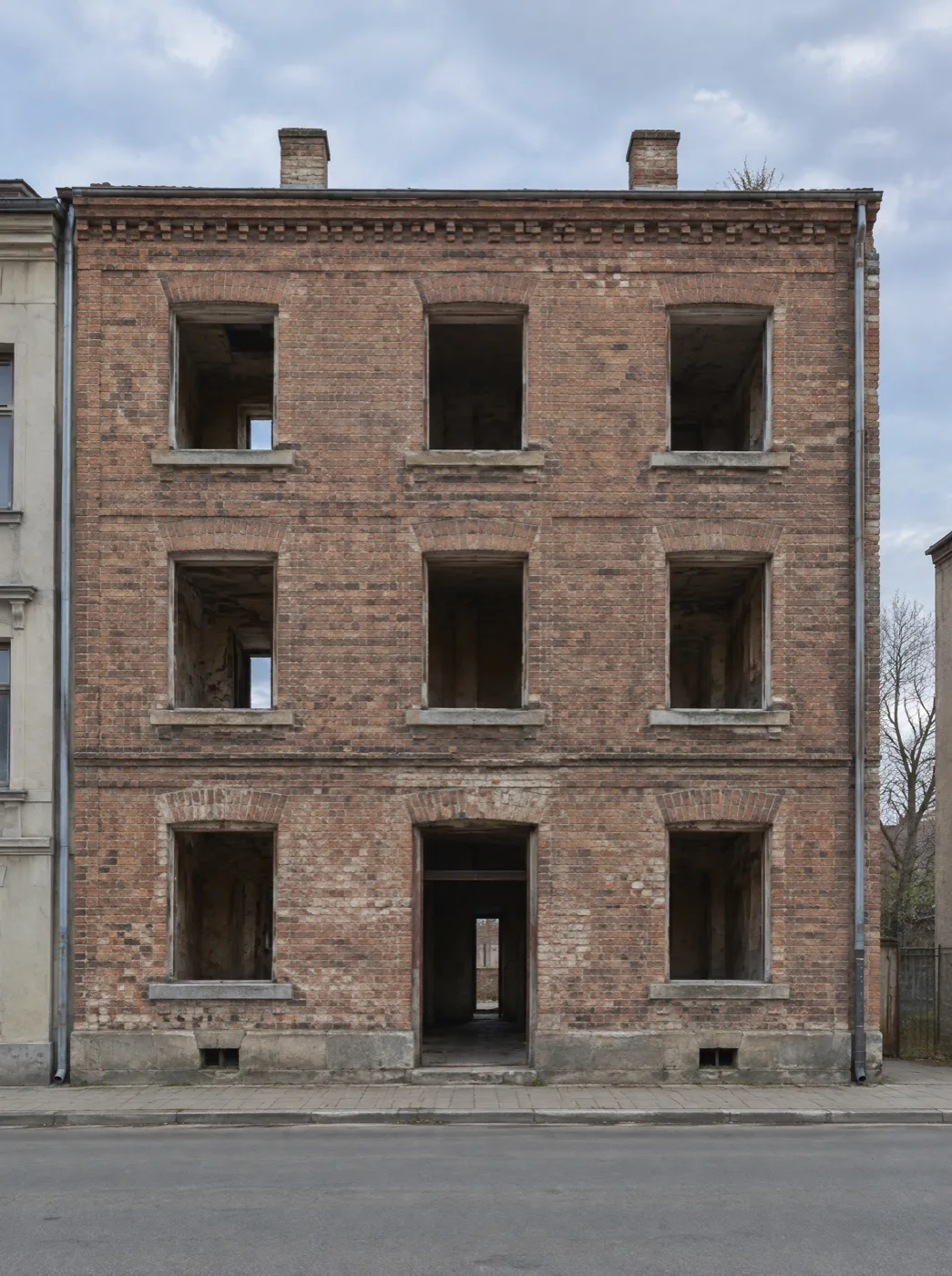 Ceglana kamienica bez stolarki okiennej, elewacja z odsłoniętą cegłą, widok od ulicy